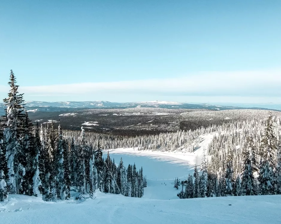 View down a snowy ski run overlooking a frozen lake and forest at Big White Ski Resort in British Columbia, Canada
