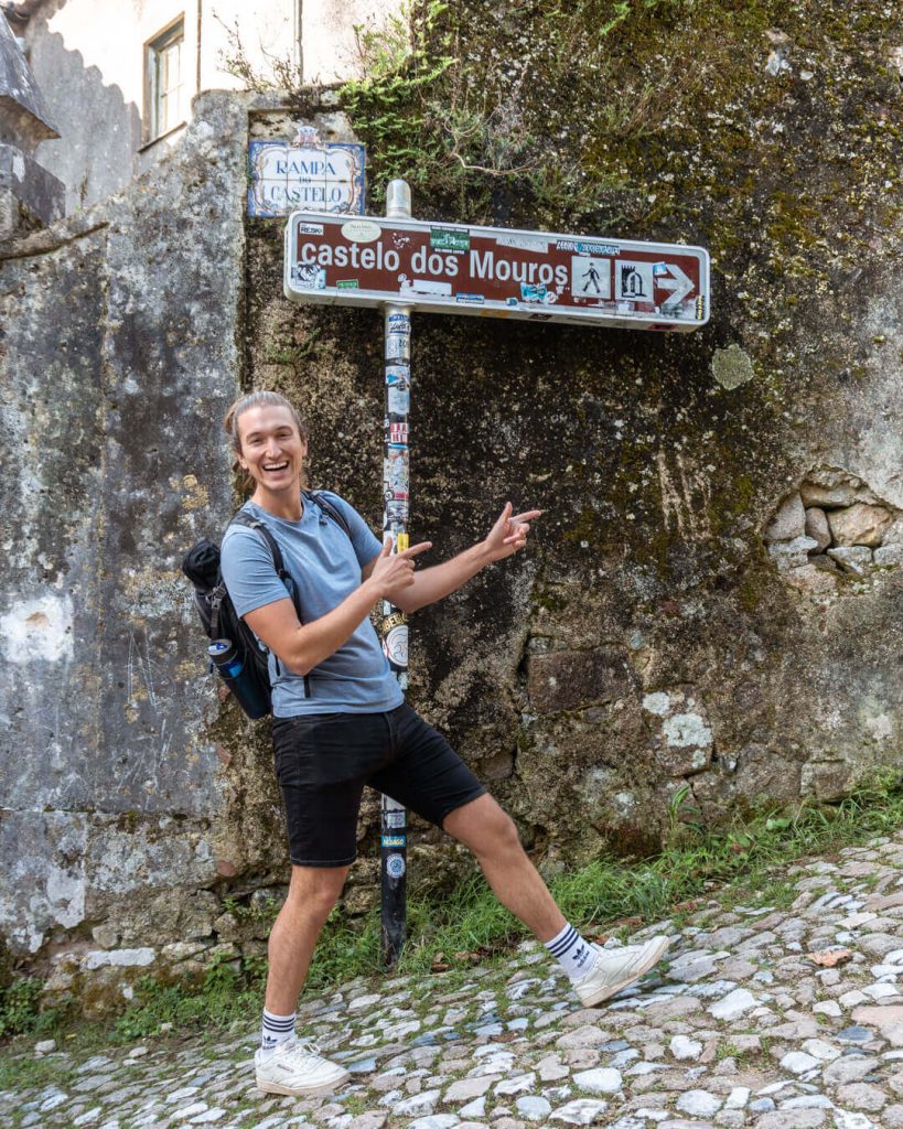 A guys standing next to a hiking sign for Castelo dos Mouros.