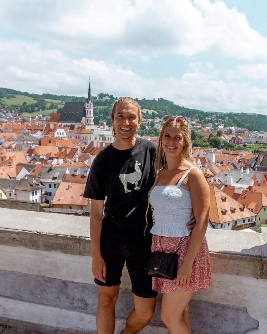 Couple standing above the town center of Cesky Krumlov. You can see all the red rooftops as well as the Church of St. Jakub Vetsi.
