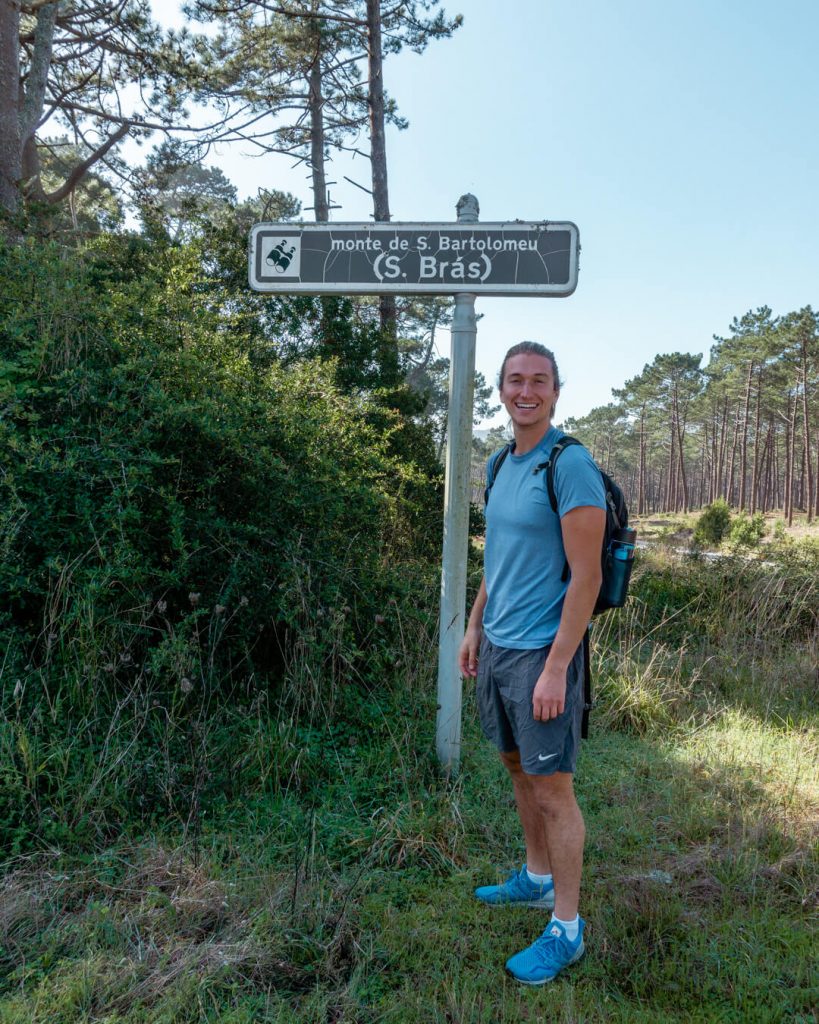 A man standing next to the trailhead up to Monte S Bartolomeu.