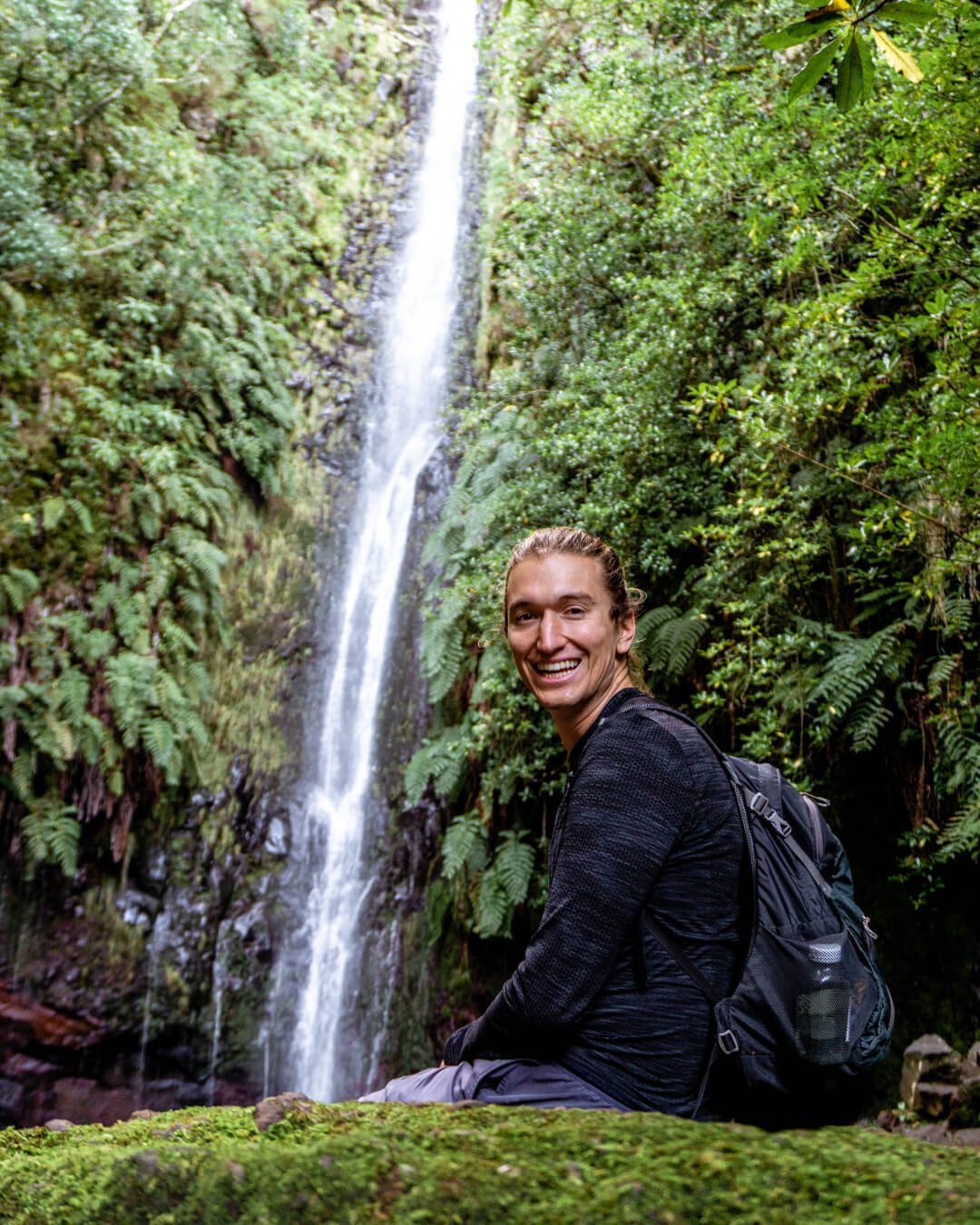 A man sitting in front of the 25 Levada Waterfall.