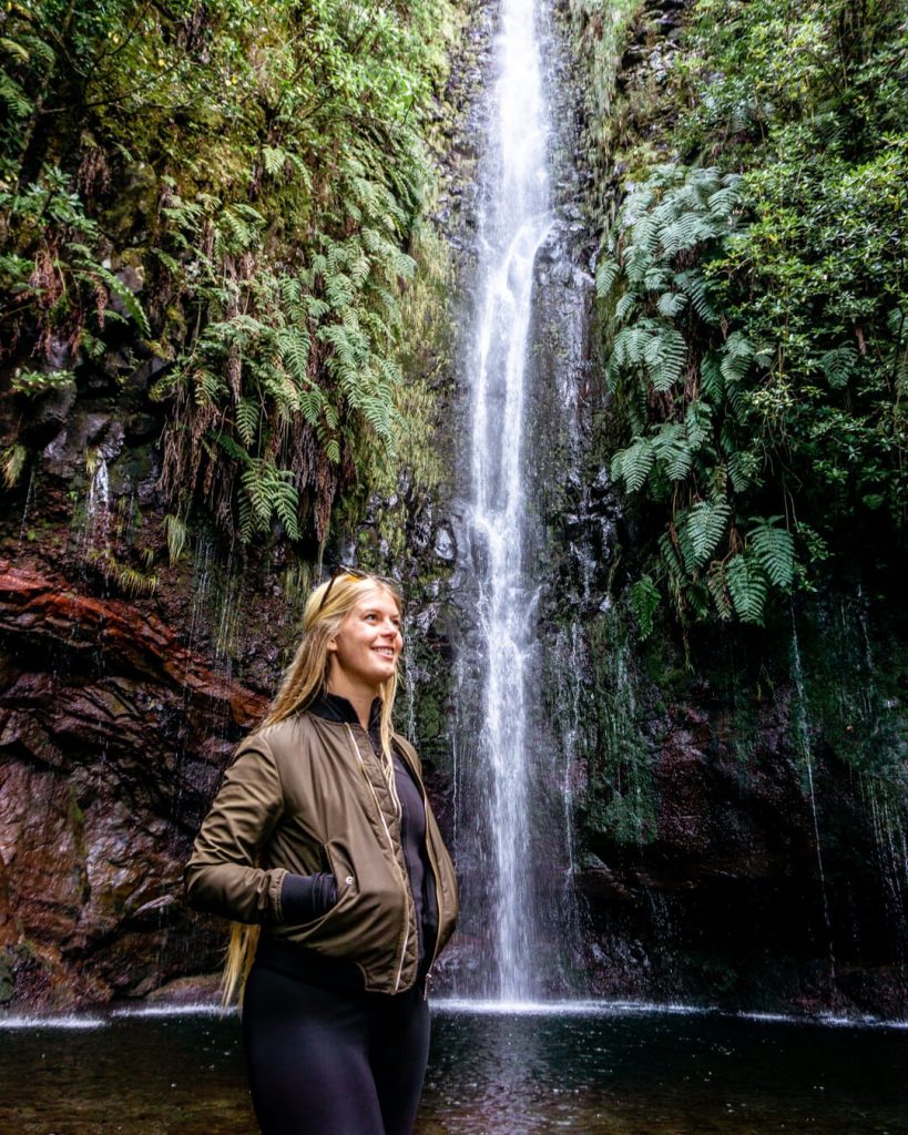 A girl smiling next to the 25 Fontes waterfall in Madeira.