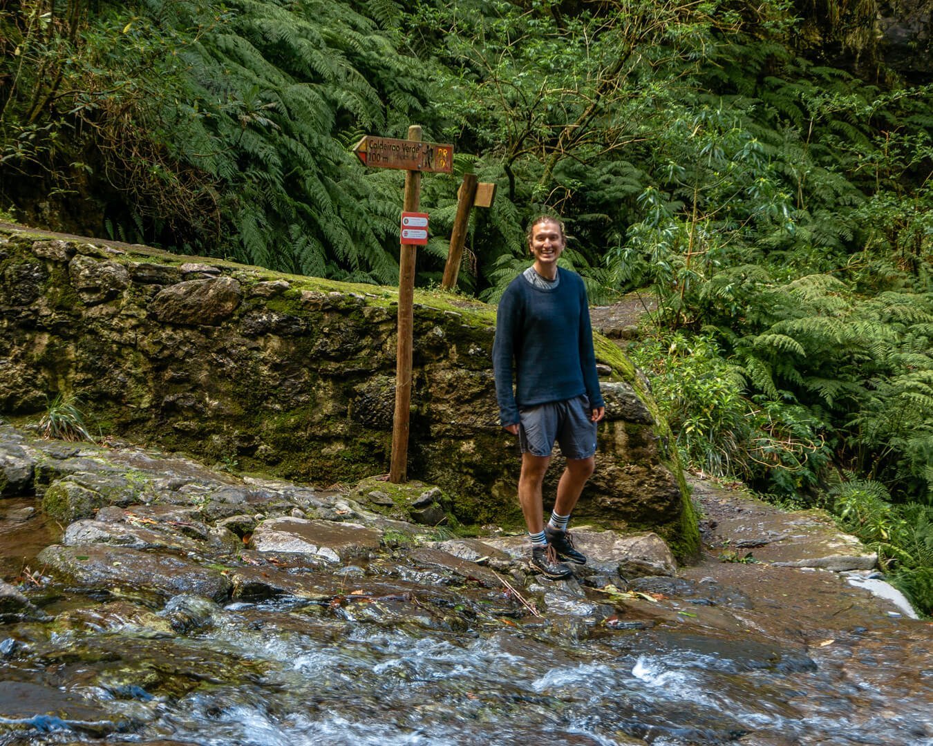 Guy standing in front of running water next to a trail sign in Madeira