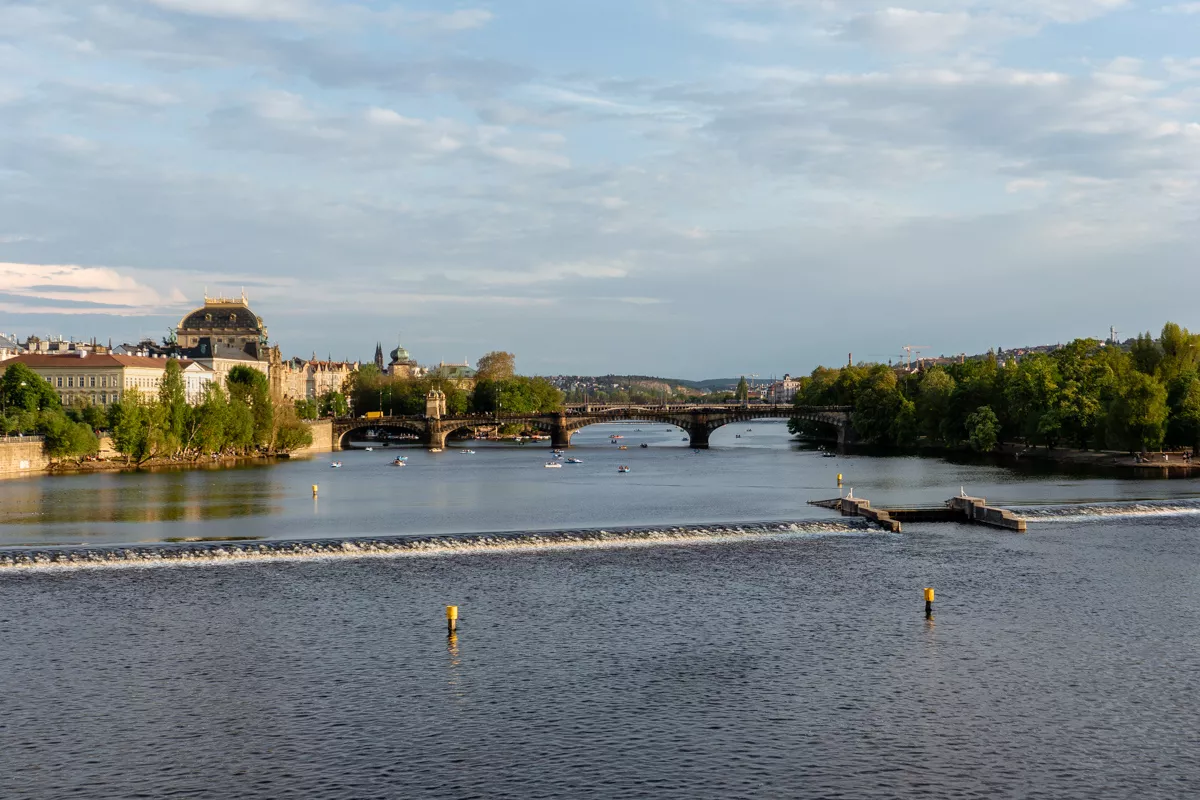 Vltava River with historic bridges and Prague’s National Theatre in the background on a sunny afternoon.