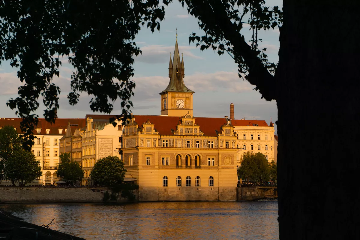 Golden hour view of the Smetana Museum building in Prague framed by trees along the Vltava River.