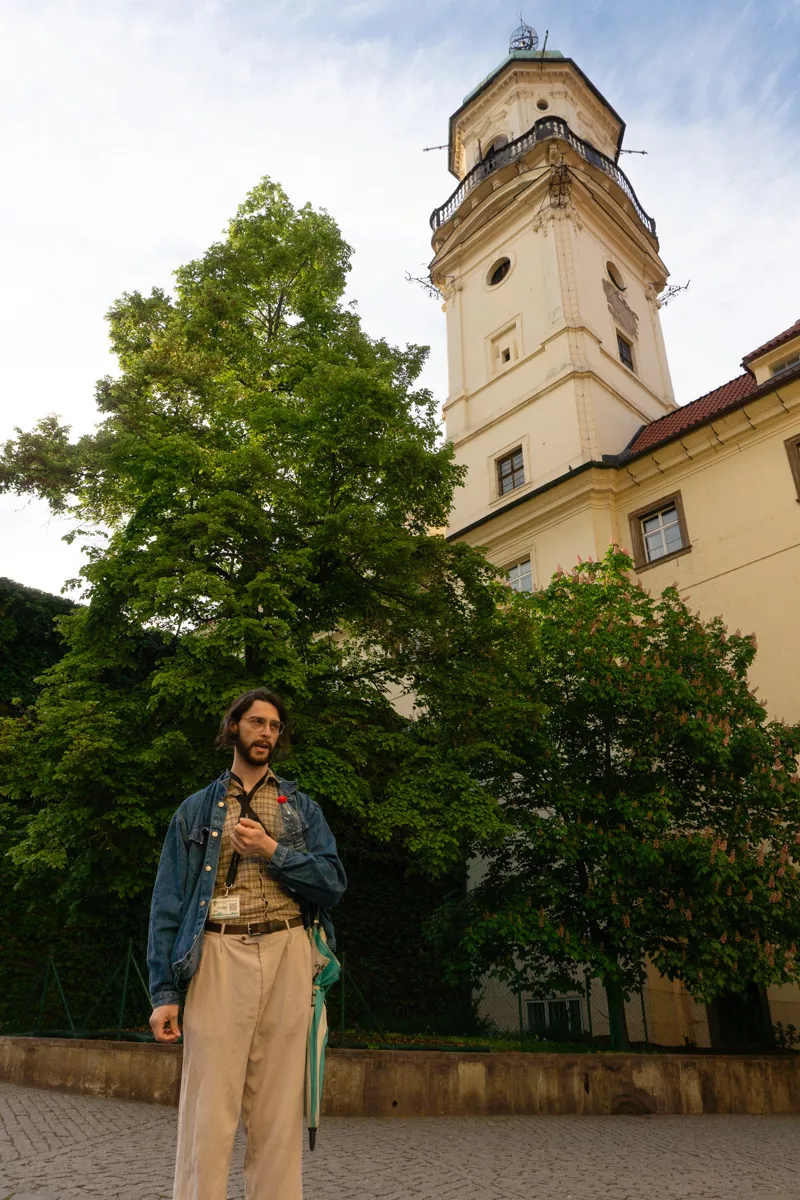 Free walking tour guide speaking in front of a historic tower in Prague during the afternoon.