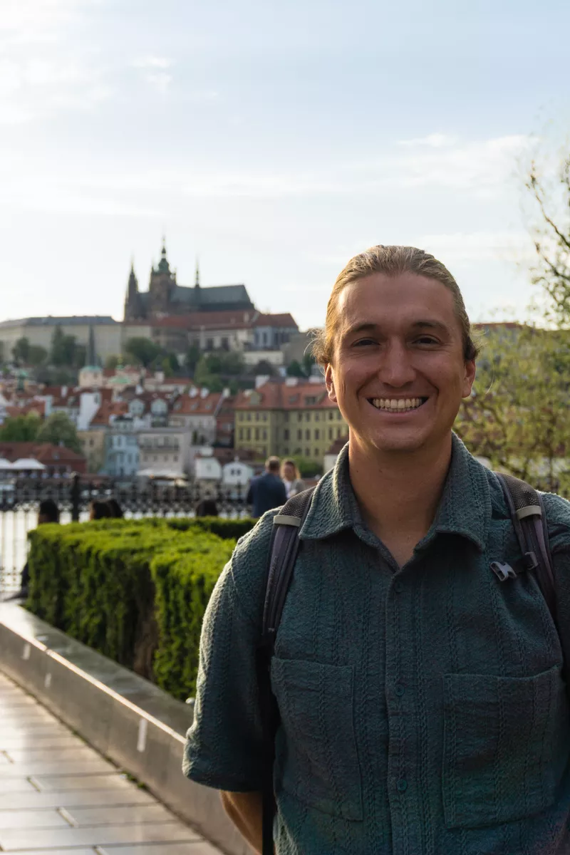 Happy tourist smiling with Prague Castle and red rooftops in the background.