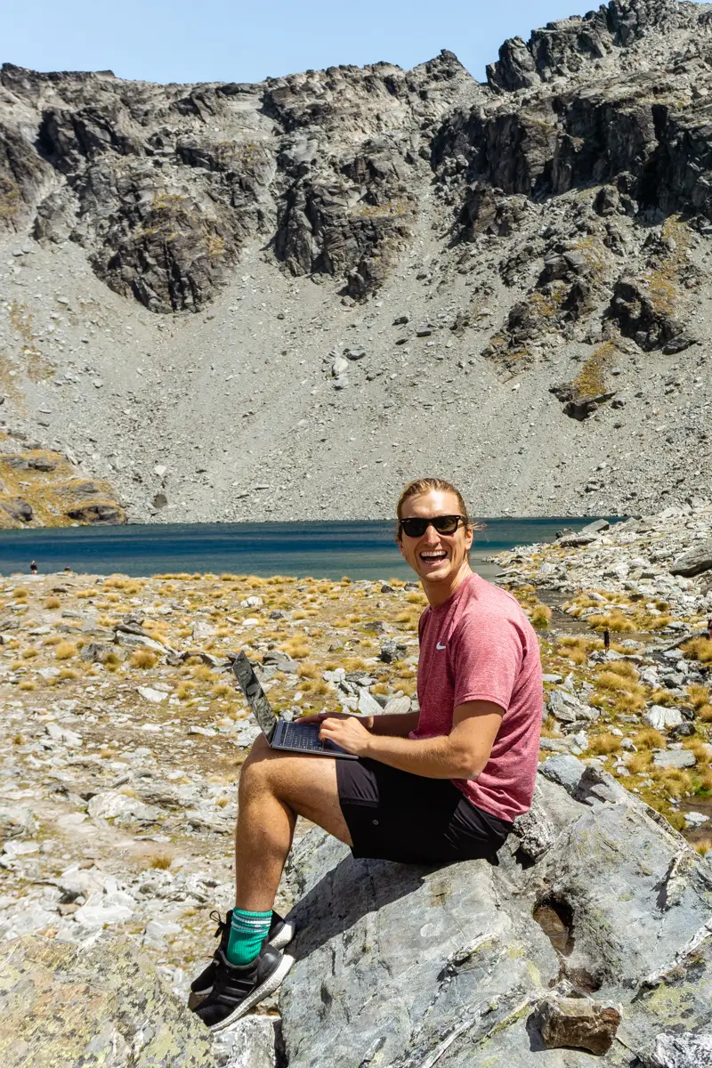 Dom working on his laptop in front of Lake Alta, a beautiful mountain lake near Queenstown in New Zealand.