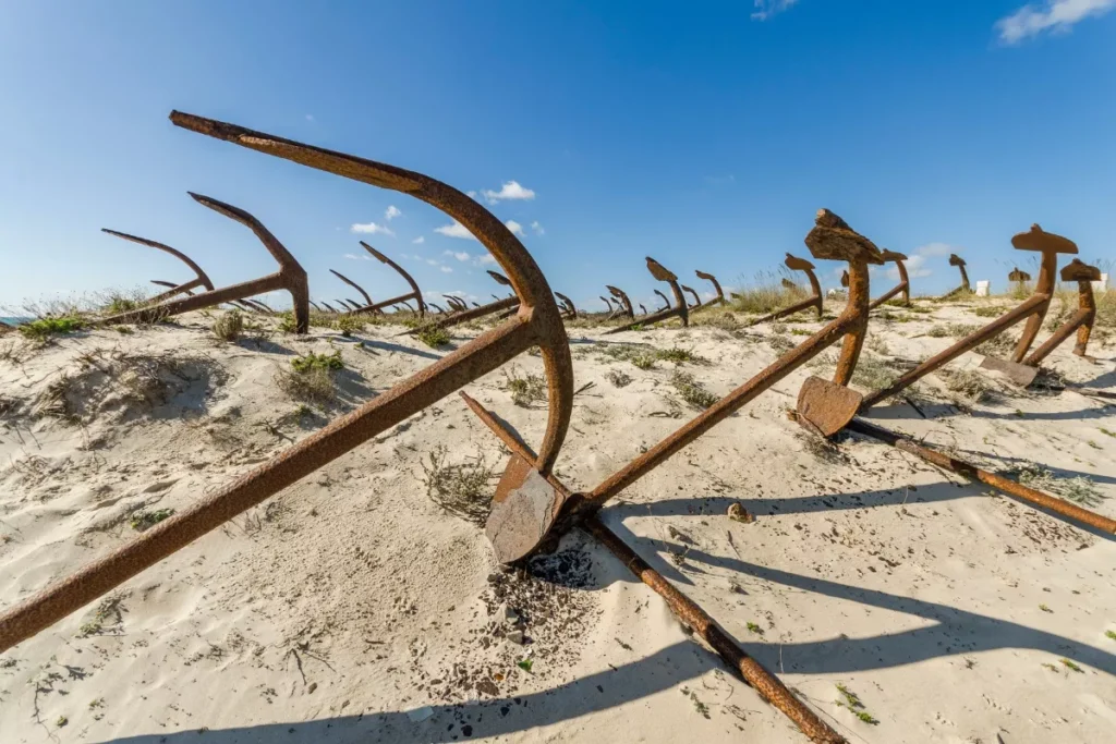 An anchor graveyard on a white sand beach in the Algarve in Portugal. The sky in the background is blue with very few clouds.