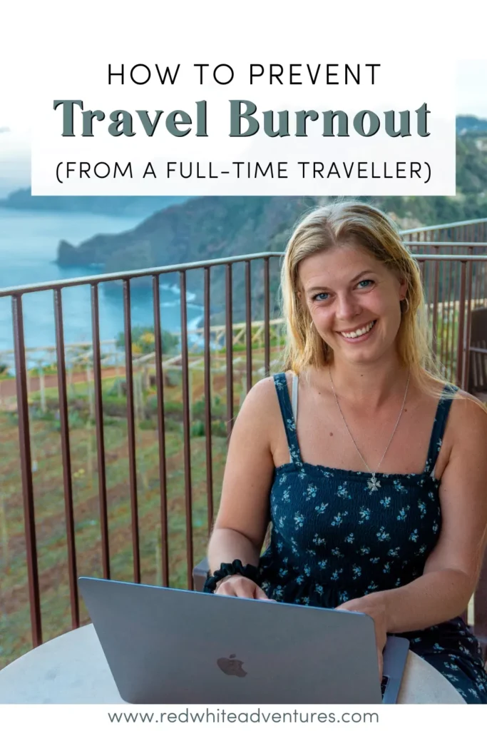 A blonde woman in a dark blue floral dress smiles while working on a laptop at a table on a balcony with ocean cliffs in the background in Madeira. The text reads “How to Prevent Travel Burnout (From a Full-Time Traveller).”