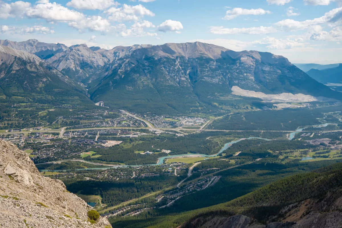 A broader panoramic perspective of Canmore, showing the full stretch of the valley, forested ridges, and the dramatic mountains that dominate the skyline.