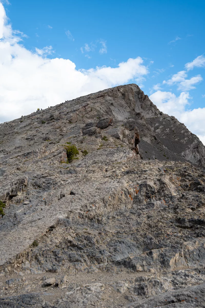 A close-up of Ha Ling Peak's rugged cliffs, showcasing the striking vertical rock faces and sharp contours under a sky filled with dynamic clouds.