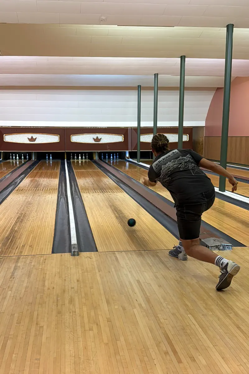 Person bowling at a retro-style bowling alley in Revelstoke, releasing a bowling ball down the wooden lane.