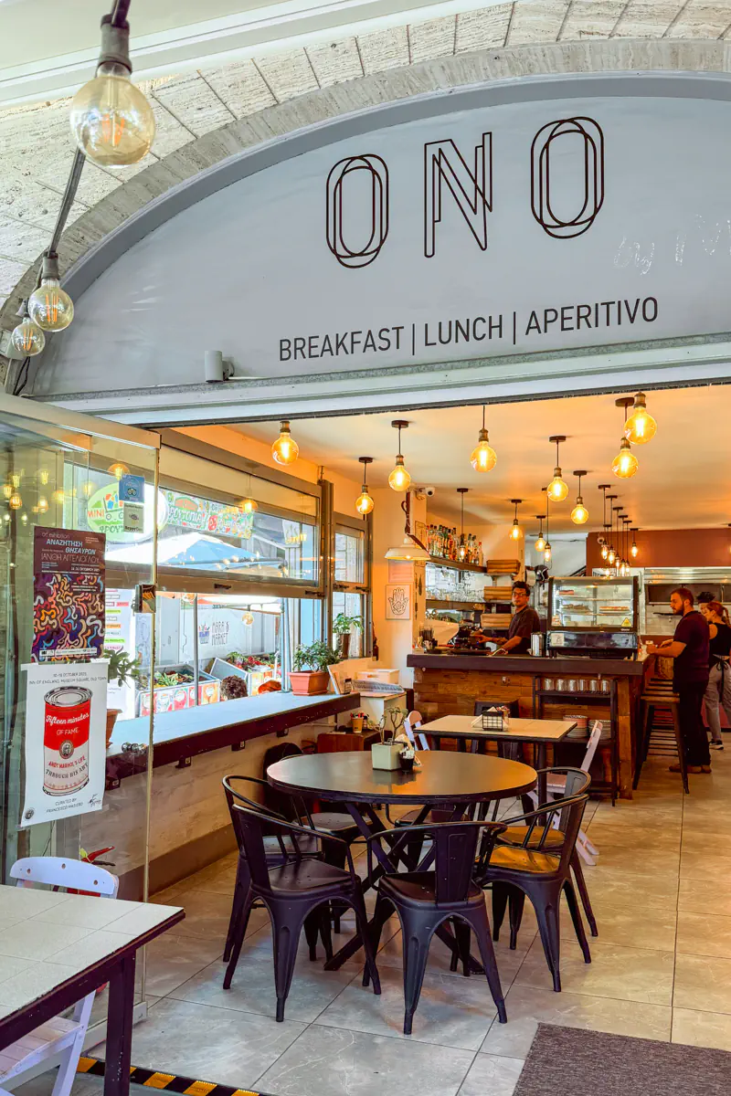 The entrance to ONO café in Rhodes, a cozy eatery with industrial-style lighting and a sign above the door reading “Breakfast | Lunch | Aperitivo.”