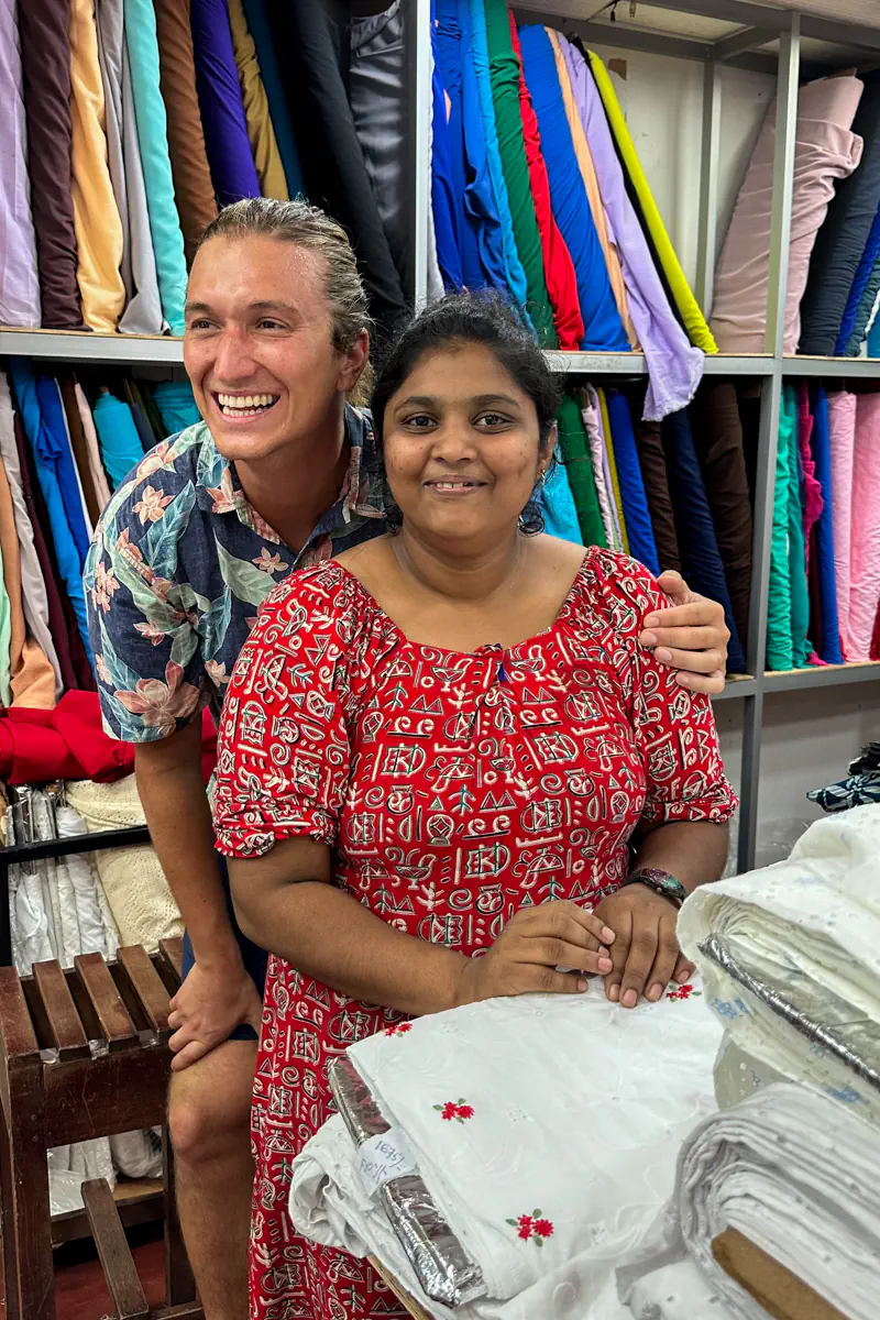 A smiling man and a local woman pose together inside a vibrant fabric store in Galle lined with colourful bolts of cloth.