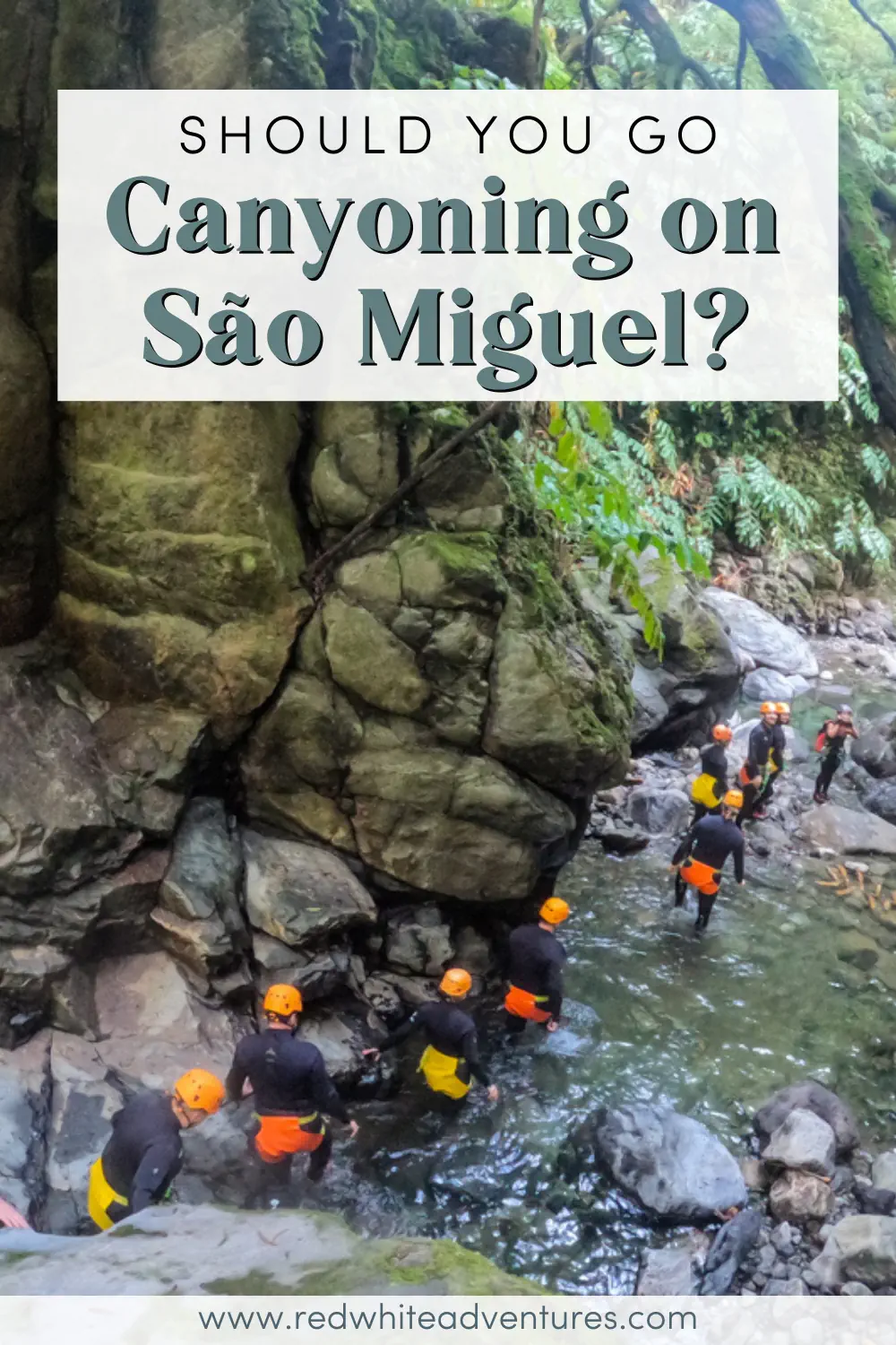 A group of canyoning participants walk through a narrow rocky stream surrounded by steep canyon walls and greenery. Text overlay asks, “Should you go canyoning on São Miguel?”