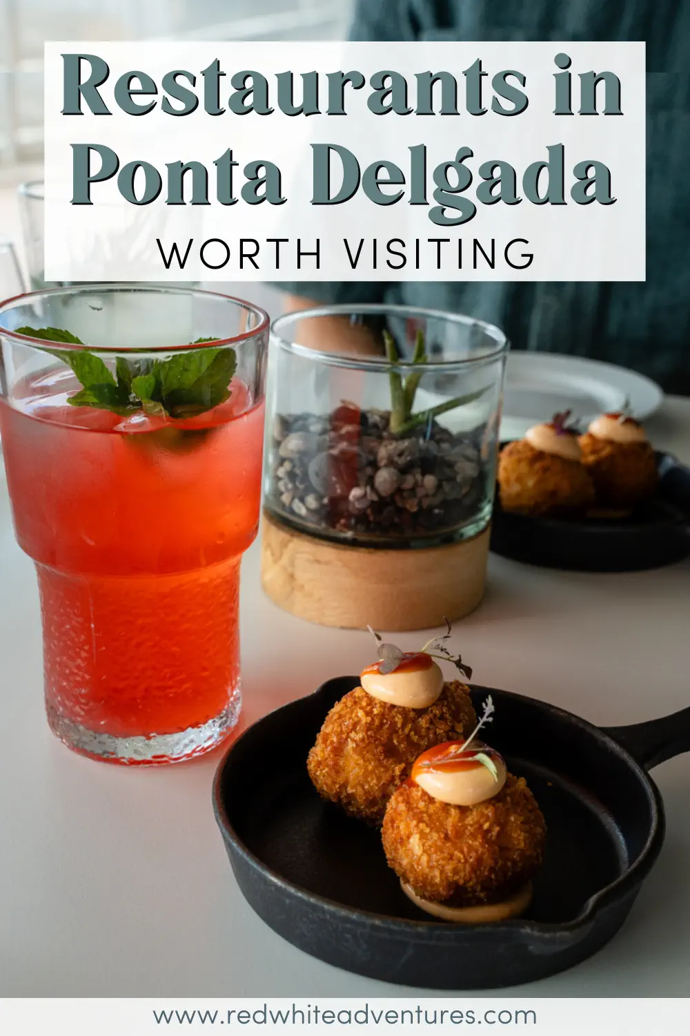 Two fried croquettes served in a small black pan sit on a table beside a pink lemonade drink garnished with mint and a glass planter. Text over the image reads “Restaurants in Ponta Delgada Worth Visiting.”