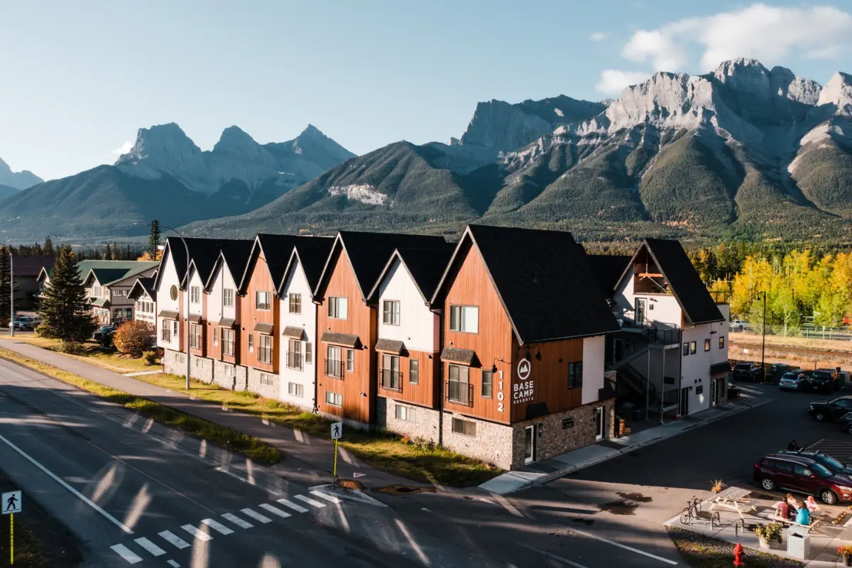 Basecamp Resorts building in Canmore, Alberta, with modern alpine-style architecture along a street and rugged mountain peaks rising in the background under a clear sky.