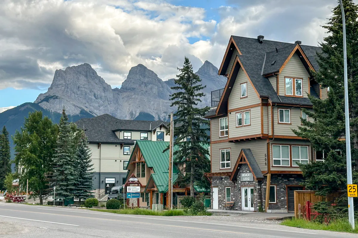 Street view of Bow Valley Trl in Canmore, Alberta, with mountain peaks rising behind lodge-style buildings and homes.