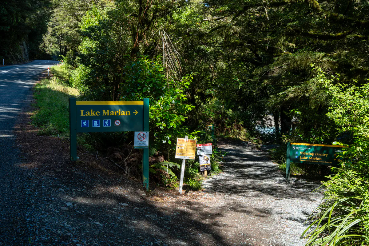 Trailhead sign for the Lake Marian hike in Fiordland National Park, New Zealand. The sign marks the start of the forest trail leading to Lake Marian.