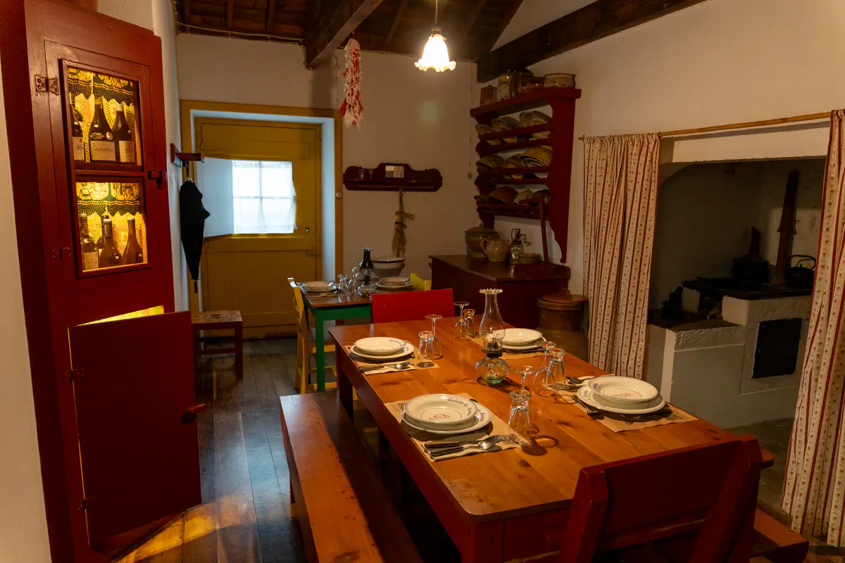 Rustic dining room with a long wooden table set with plates and glasses beside a traditional fireplace and antique wooden furniture in an Azorean home.
