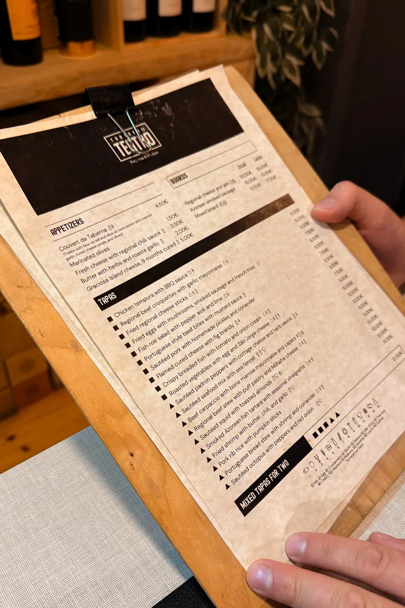 Restaurant menu showing appetizers, tapas, boards, and regional dishes held at the table.