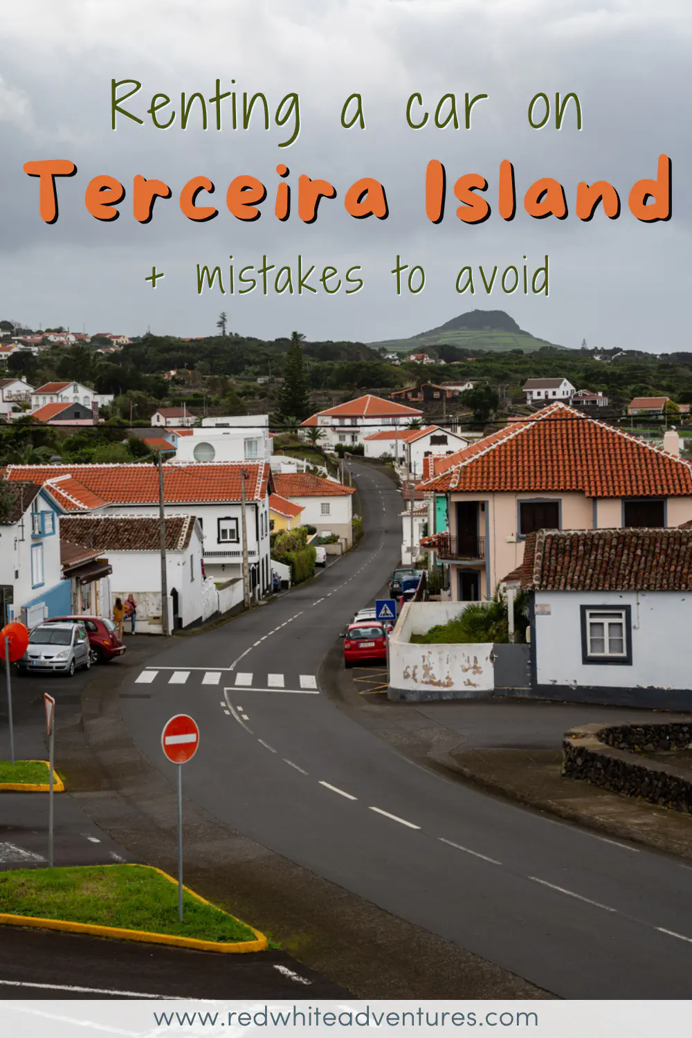 A winding road passes through a quiet village on Terceira Island in the Azores, lined with whitewashed houses topped with terracotta roofs and a volcanic peak rising in the distance under a grey sky. Text overlay reads "Renting a car on Terceira Island + mistakes to avoid."