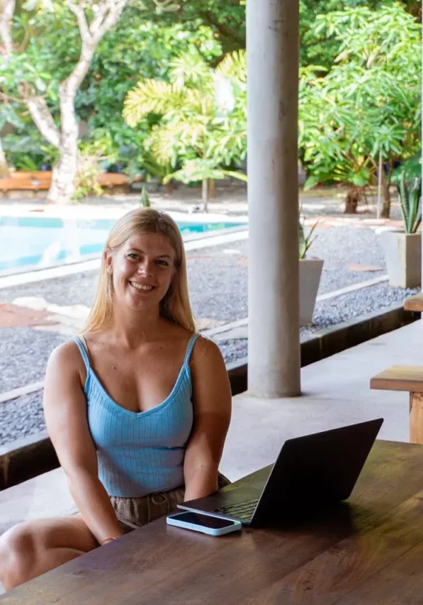 Female digital nomad smiling while working on a laptop near a poolside coworking space in Sri Lanka — tropical remote work lifestyle.