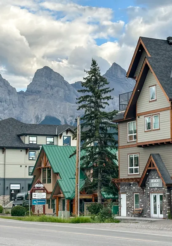 Street view of Bow Valley Trl in Canmore, Alberta, with mountain peaks rising behind lodge-style buildings and homes.