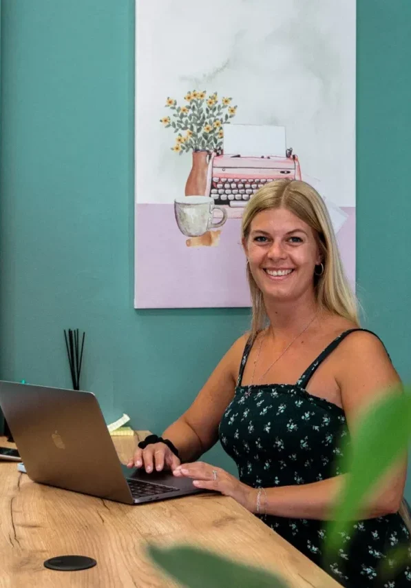 Woman sitting with her laptop at a coworking space with green wall behind her and a white painting