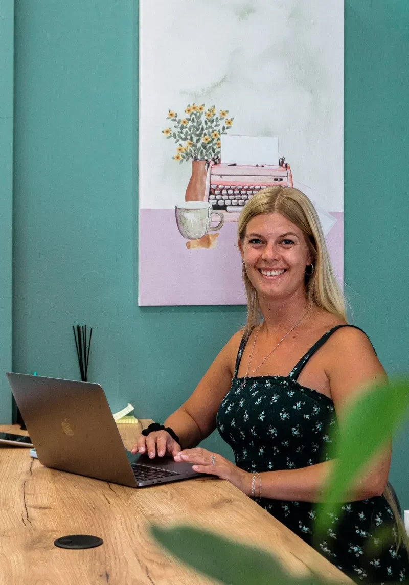 Woman sitting with her laptop at a coworking space with green wall behind her and a white painting