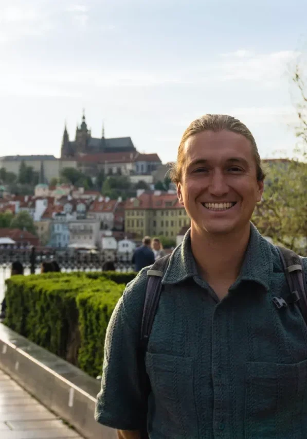 Happy tourist smiling with Prague Castle and red rooftops in the background.