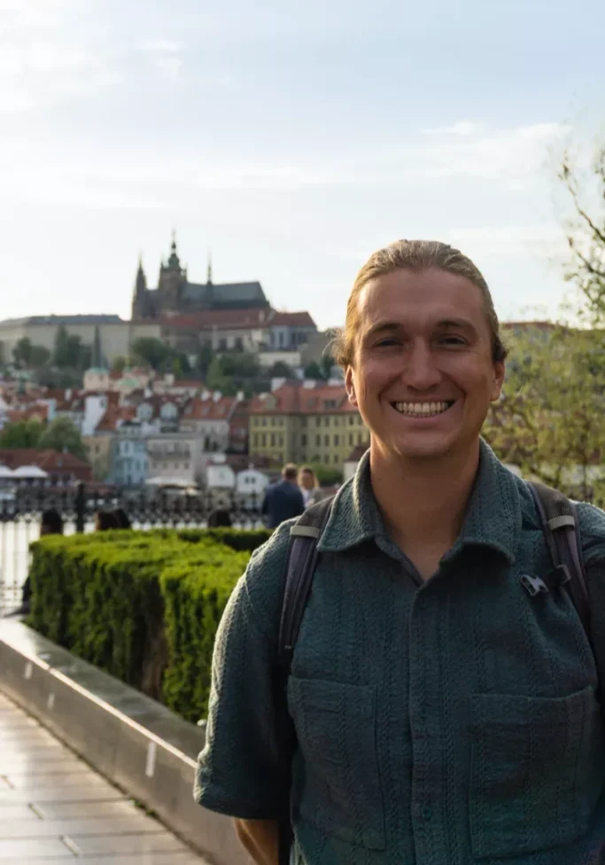Happy tourist smiling with Prague Castle and red rooftops in the background.