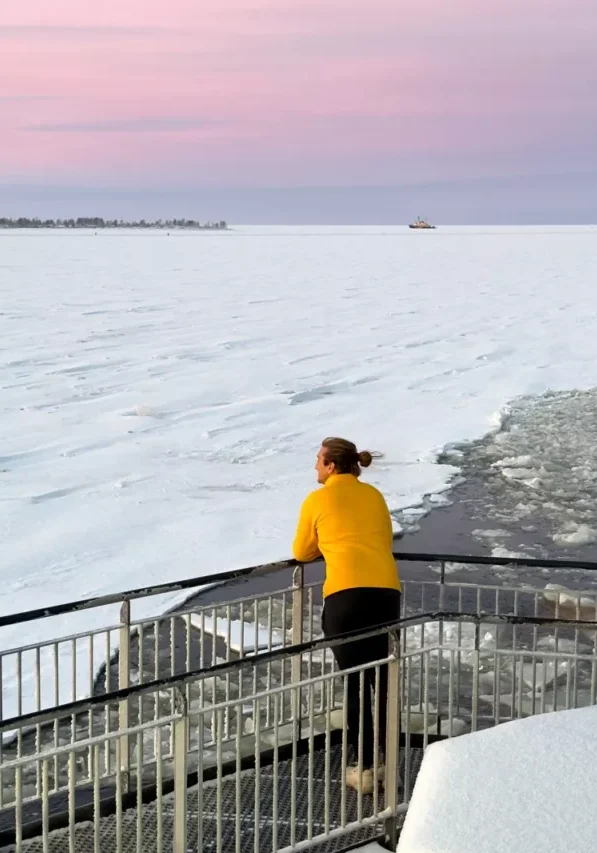 Person in a yellow sweater looking out over the frozen sea at sunrise aboard the Arktis Icebreaker in Kemi, Finland.