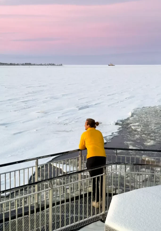 Person in a yellow sweater looking out over the frozen sea at sunrise aboard the Arktis Icebreaker in Kemi, Finland.