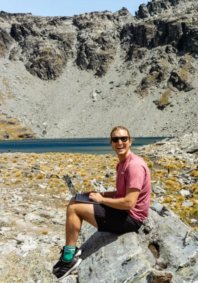 Dom working on his laptop in front of Lake Alta, a beautiful mountain lake near Queenstown in New Zealand.