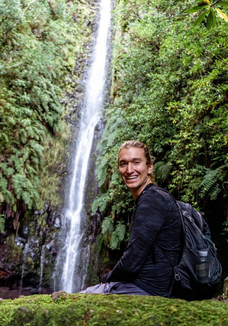 A man sitting in front of the 25 Levada Waterfall.