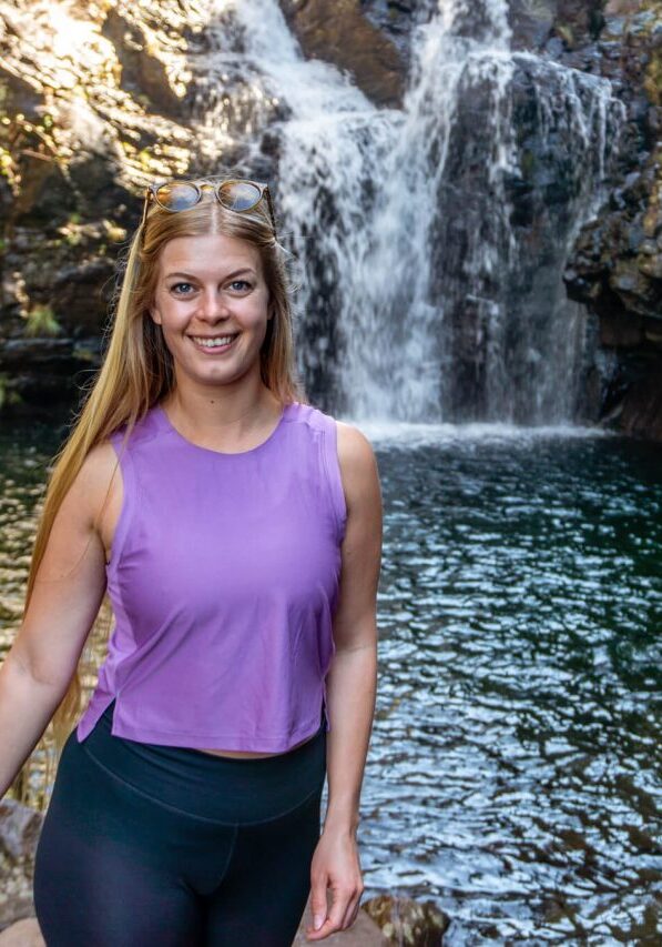 A girl standing in front of a waterfall along the Levada do Alecrim.